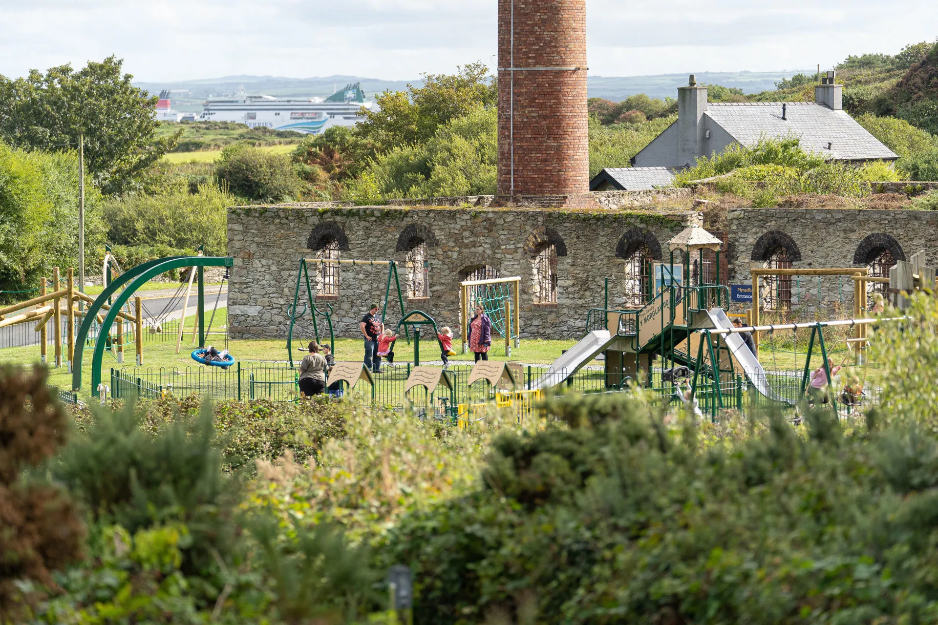 Children's play park with children on swing and outdoor gallery in the distance
