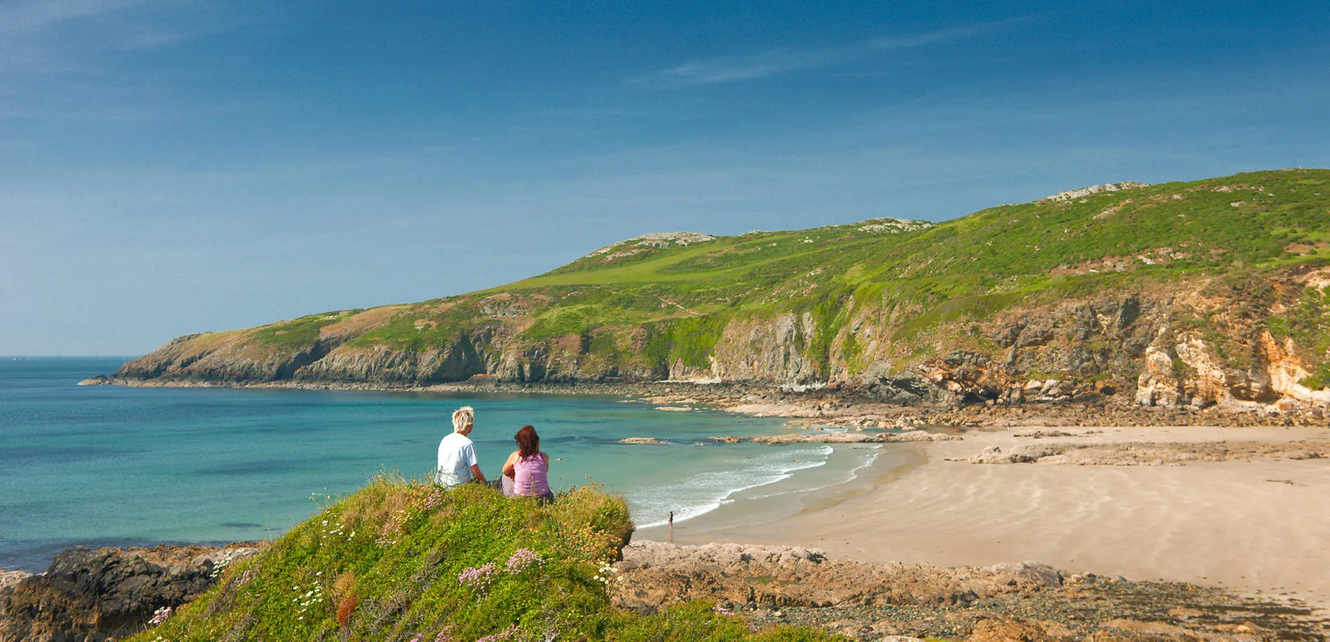 Two people sitting on the cliff looking out at the beach