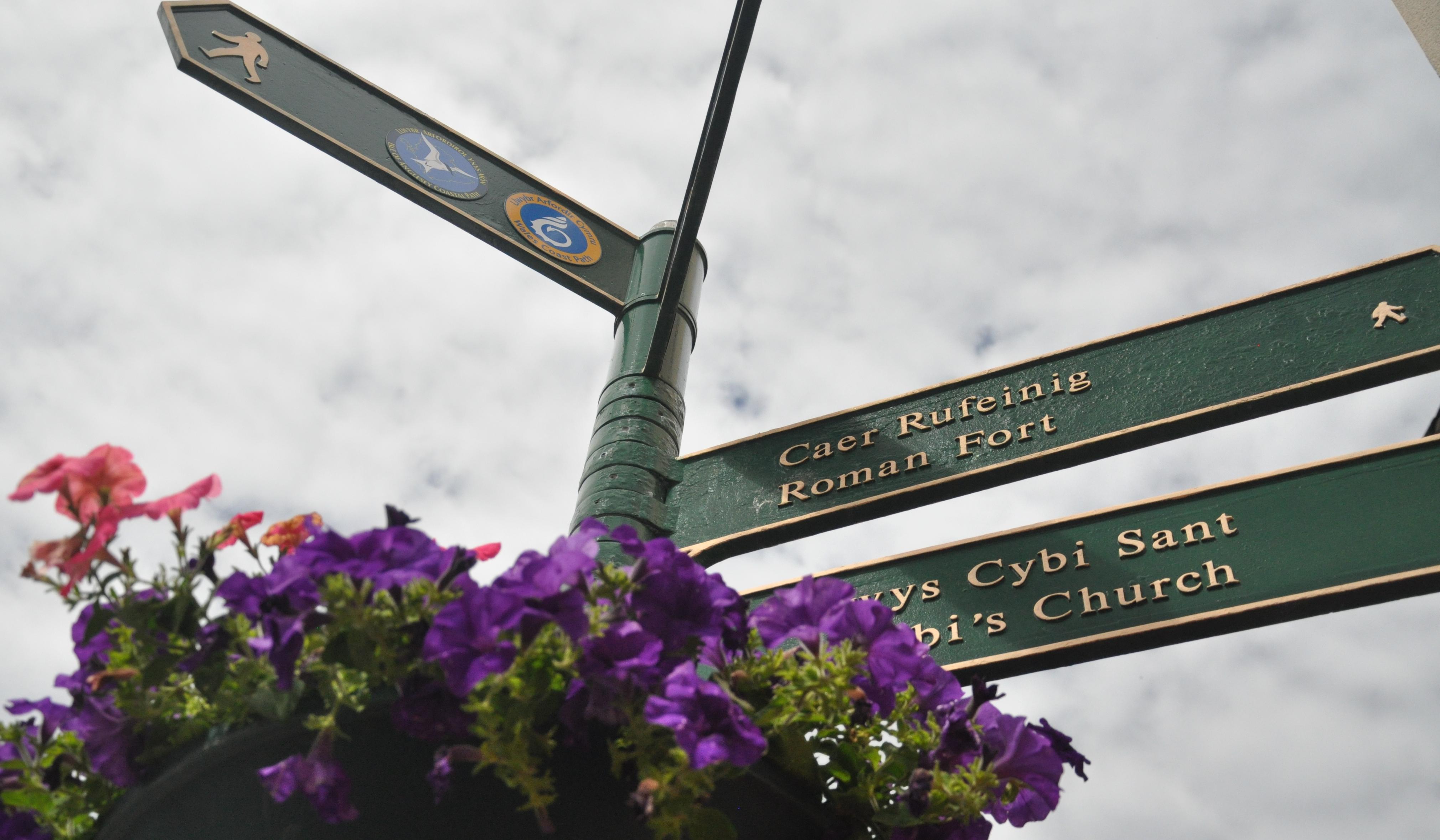 Green finger post with flowers in centre of Holyhead showing directions to Roman fort coastal path and St Cybis church