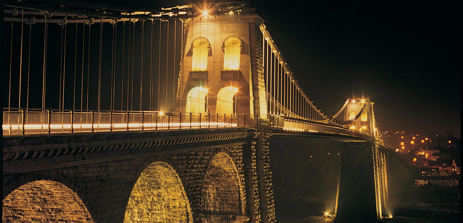 Menai Bridge at night with the pillars lit up glowing yellow