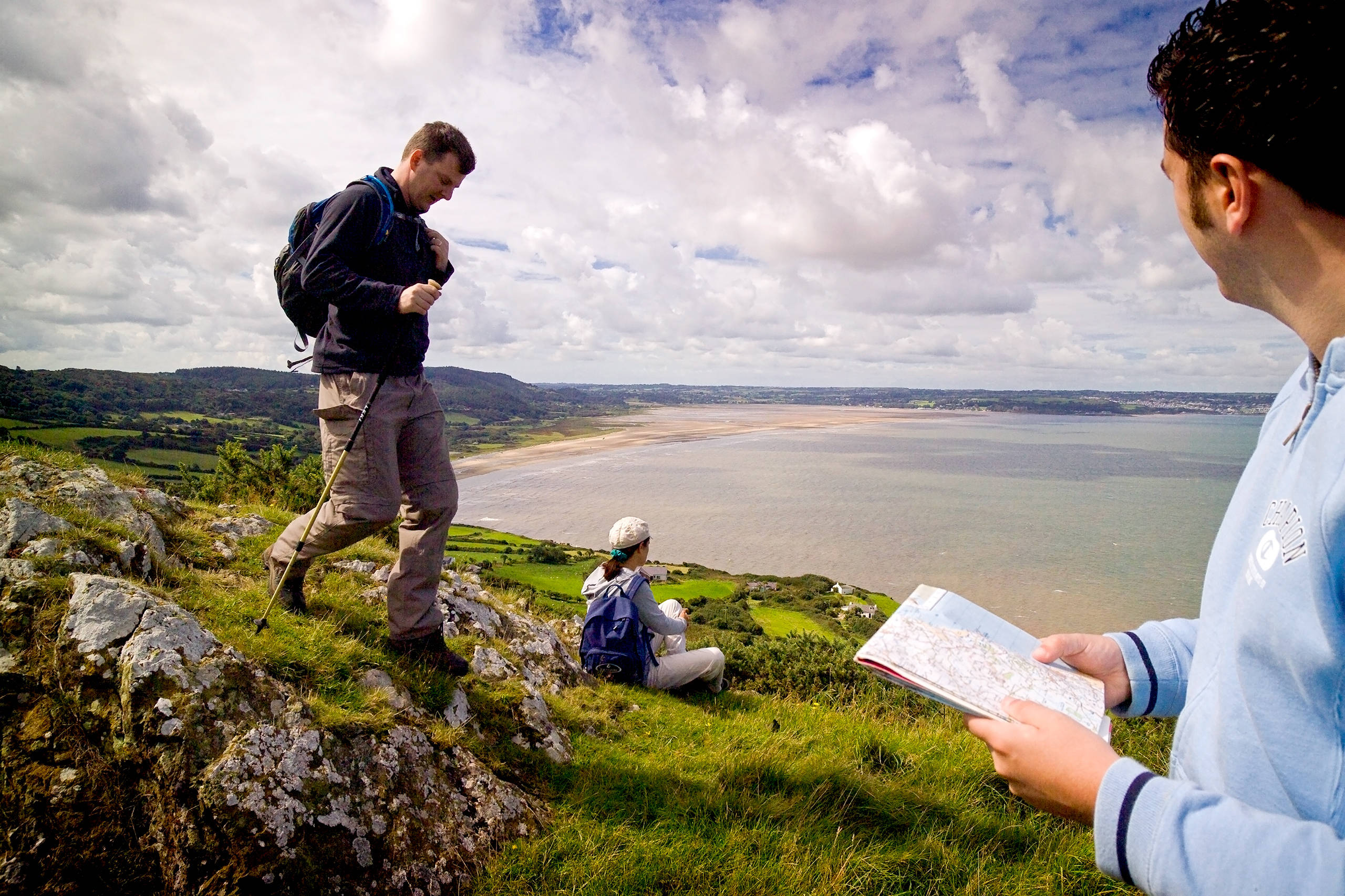 Three people walking the coast over red wharf bay with one person checking his map