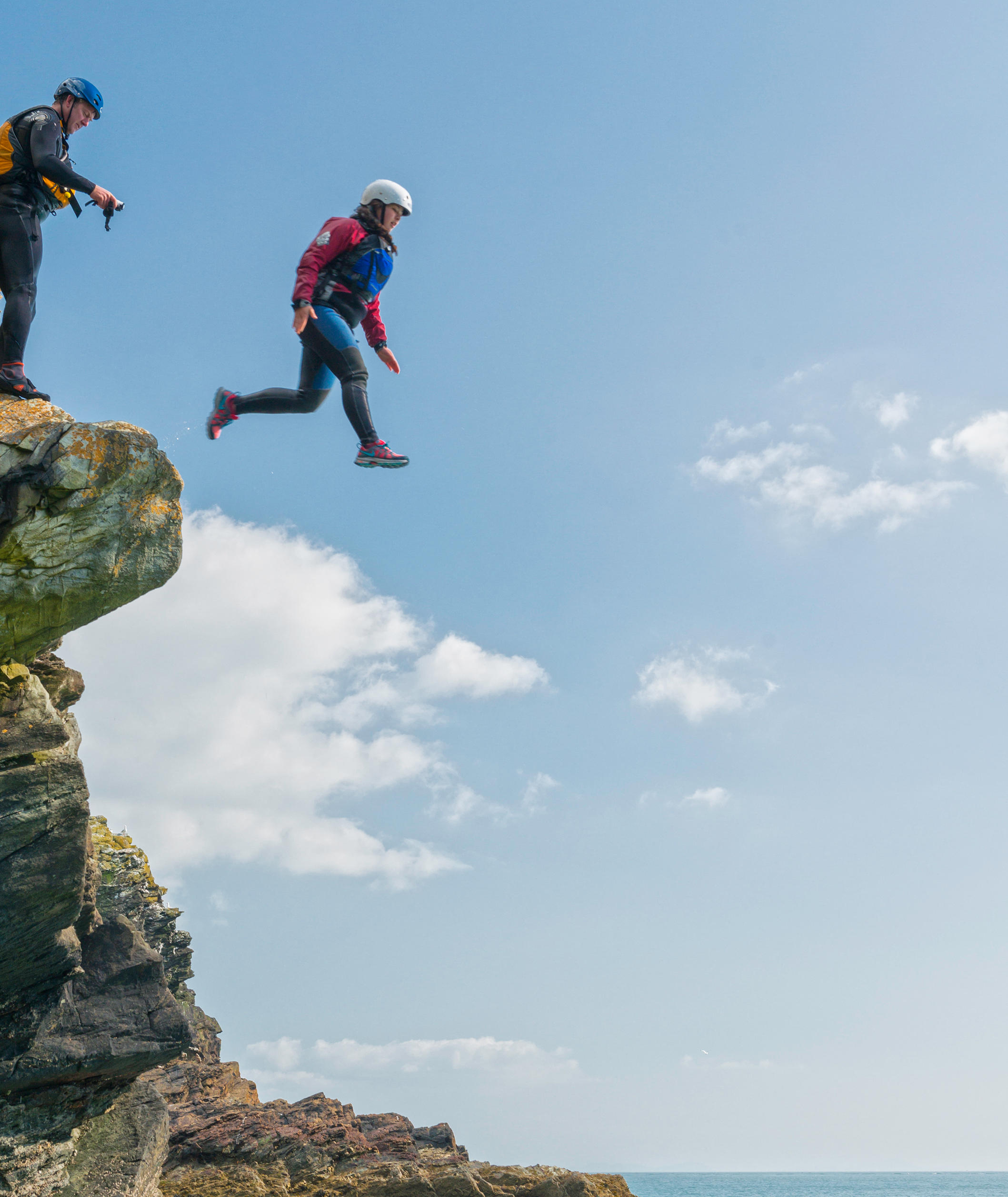 Person taking a leap of faith off cliff whilst coasteering before jumping into water
