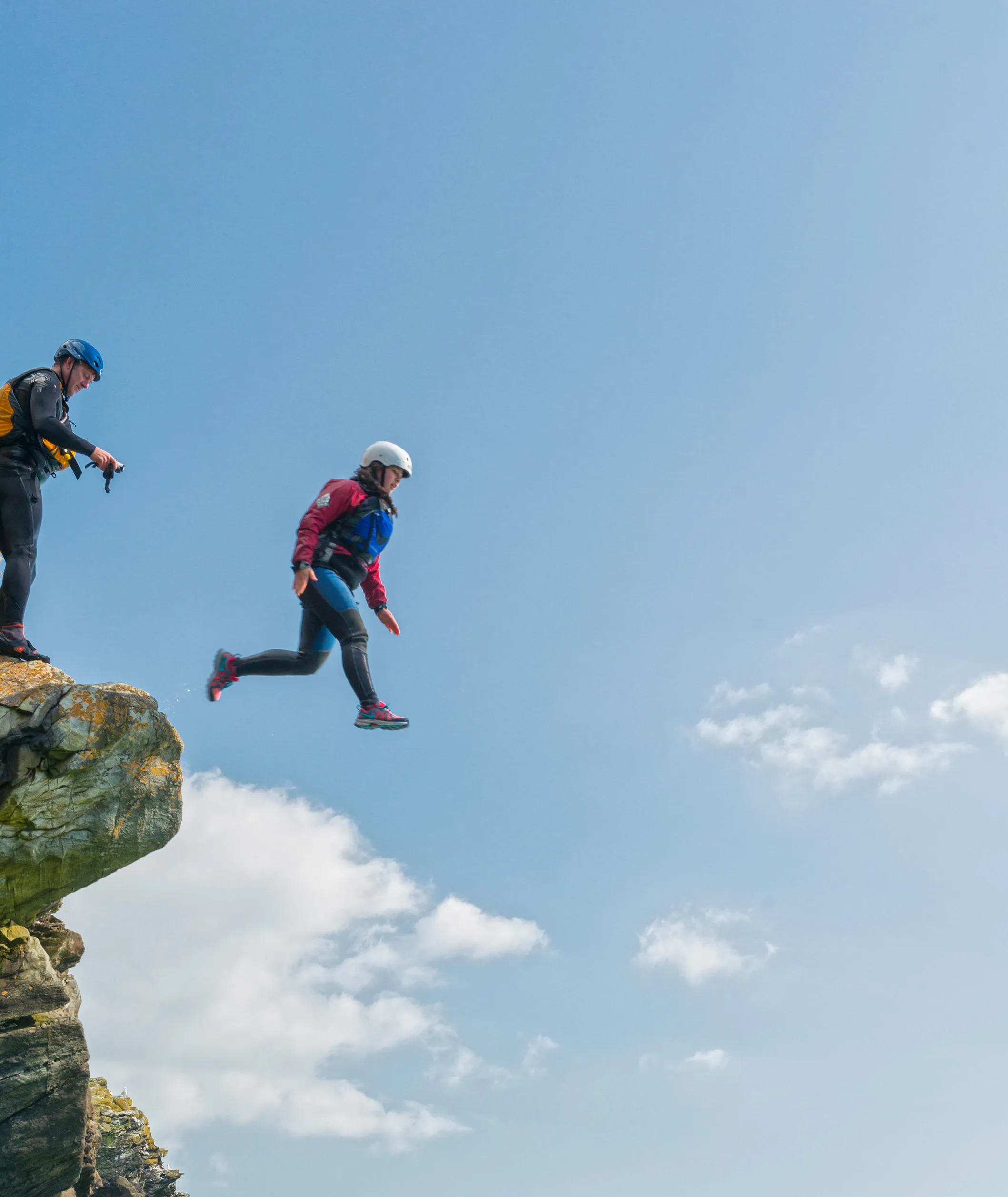 Person taking a leap of faith off cliff whilst coasteering before jumping into water