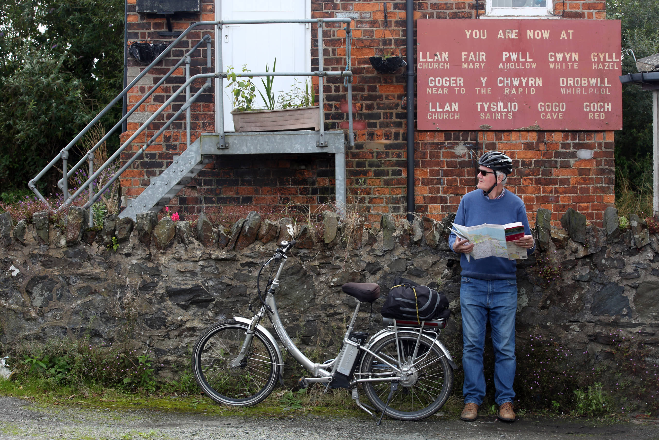 Cyclist standing next to bike checking route under railway signal box 
