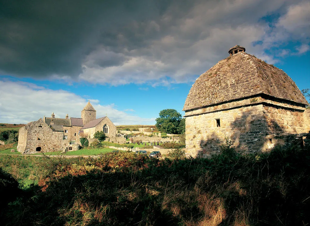 Penmon Priory under darkening stormy summer skies with the original dovecote in the foreground