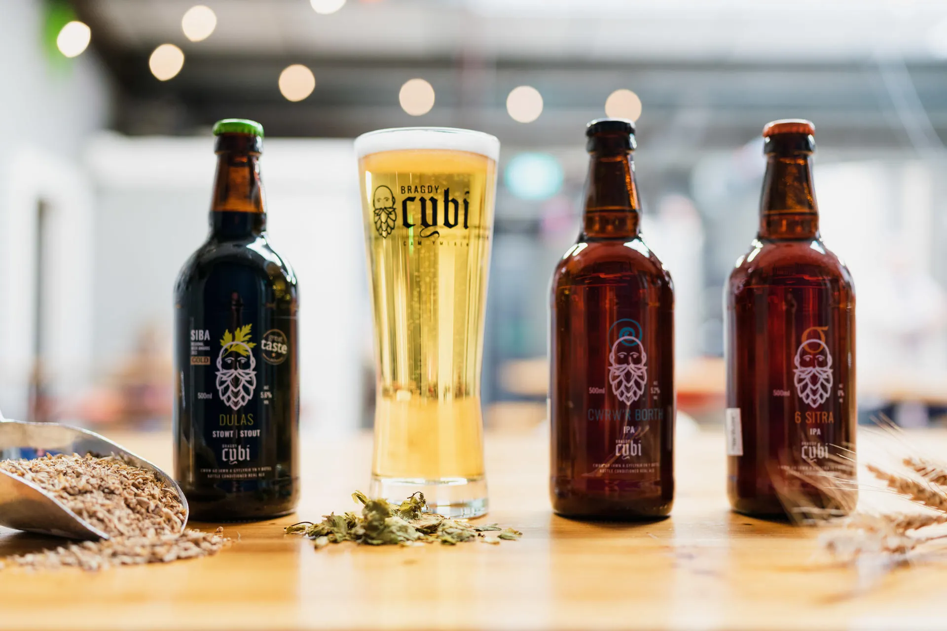 3 Bottles of beer on the bar and 1 full pint glass showing Bragdy Cybi's stout and pale ale range ready to drink.