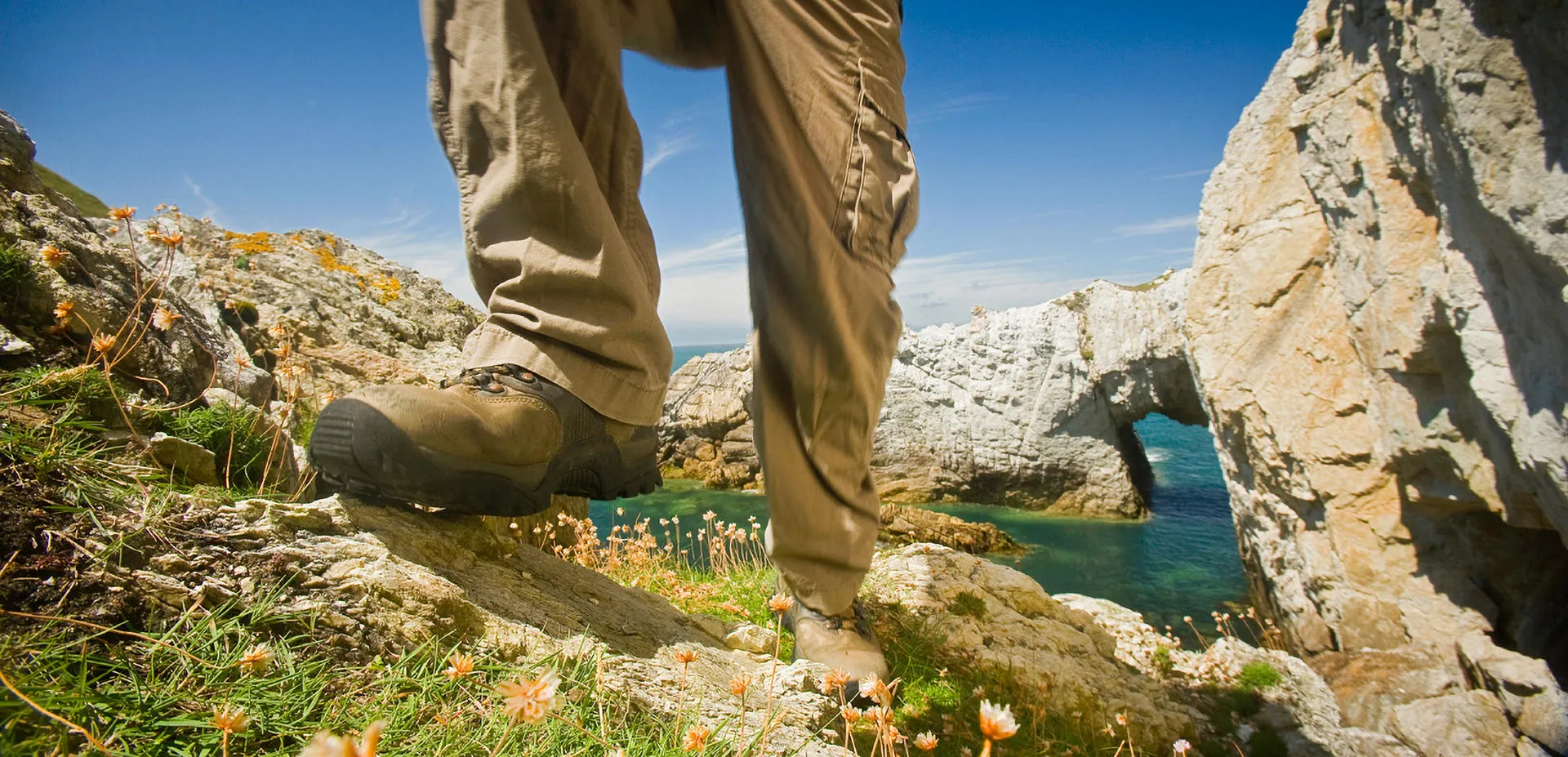 A person walking on the cliff with the Bwa Gwyn in the background on a sunny day