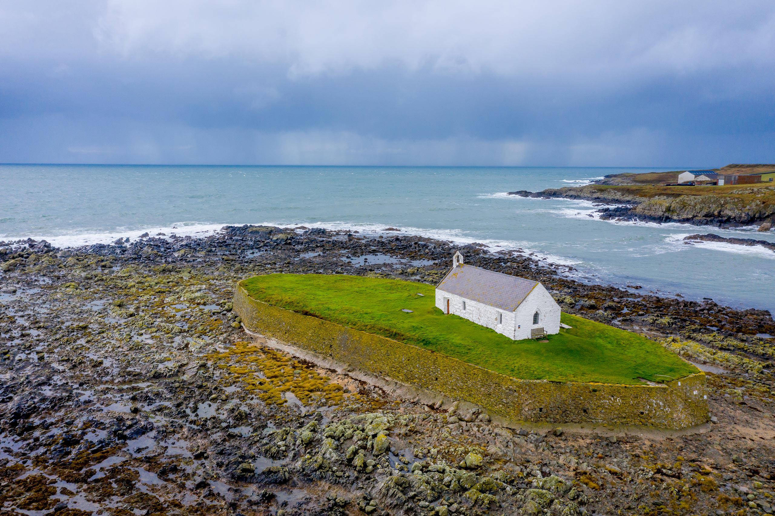 Aerial image of St Cwyfan's Church on a small tidal island surrounded by the sea