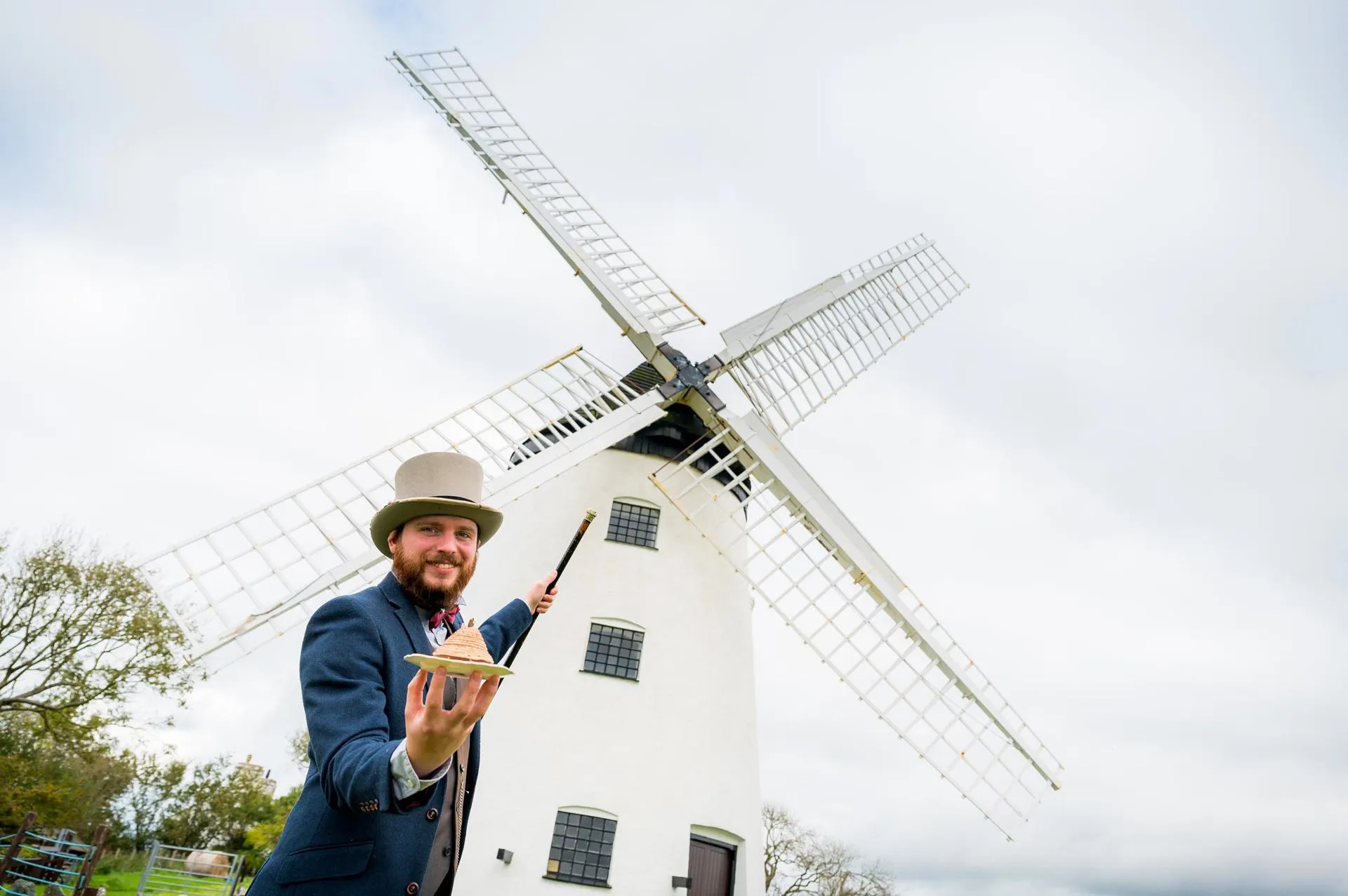 The owner of Llynon Mill presenting food and pointing at the windmill with a cane