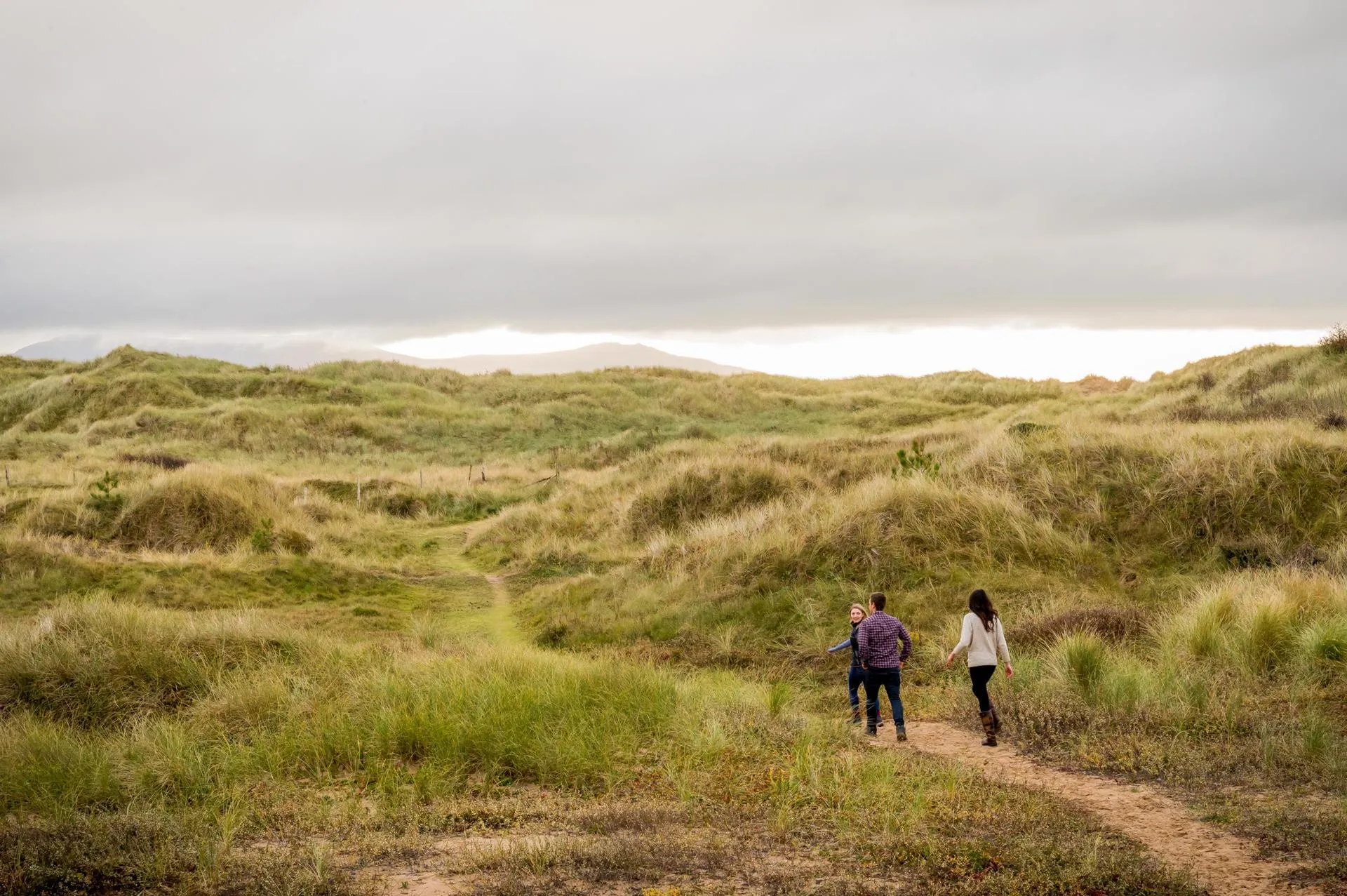 Three friends walking in the sand dunes in Niwbwrch on a cloudy day.