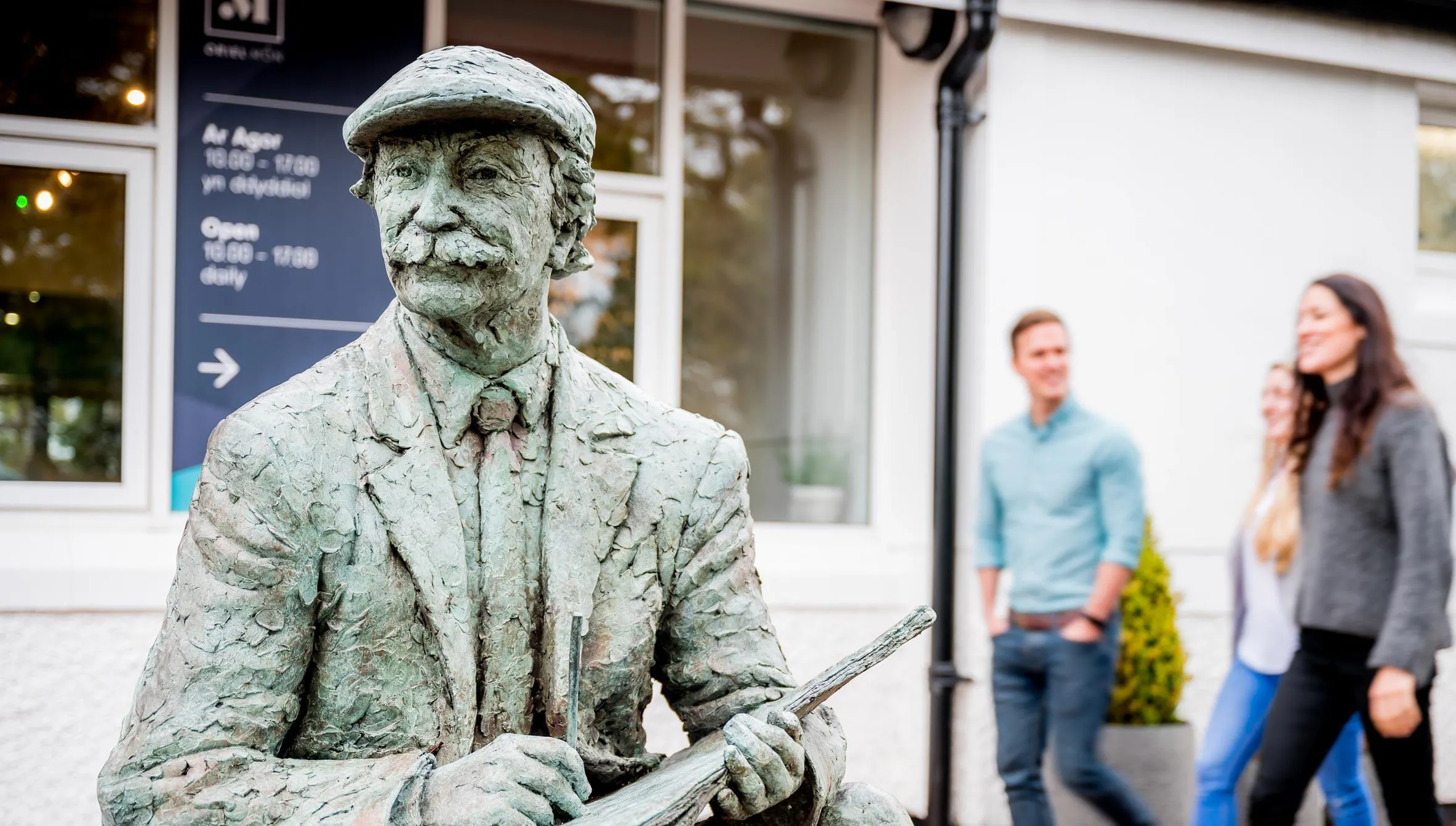 Statue of the artist Kyffin Williams outside Oriel Môn with people walking in the background