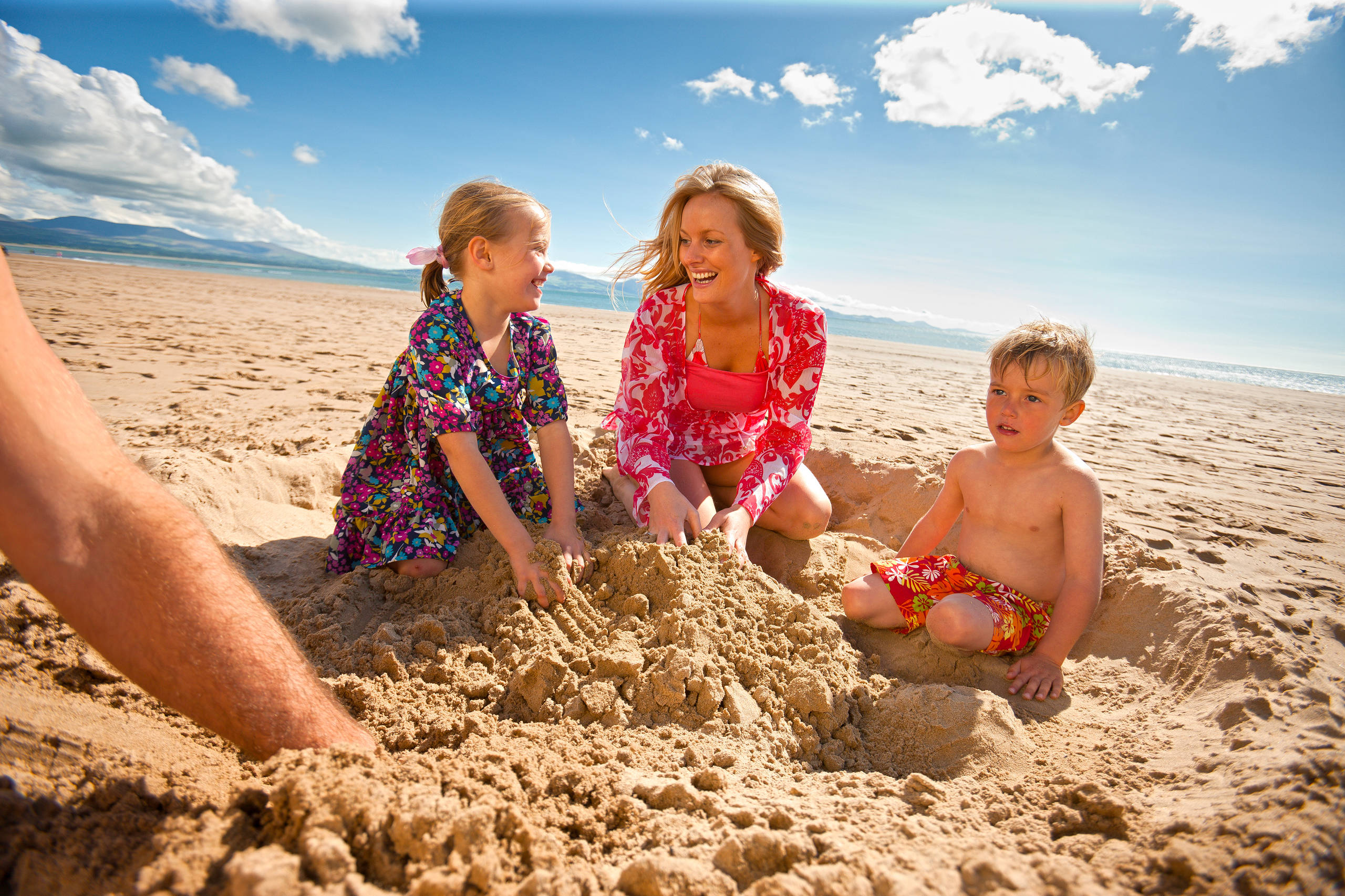 Family of 3 people playing in the sand creating a sand castle