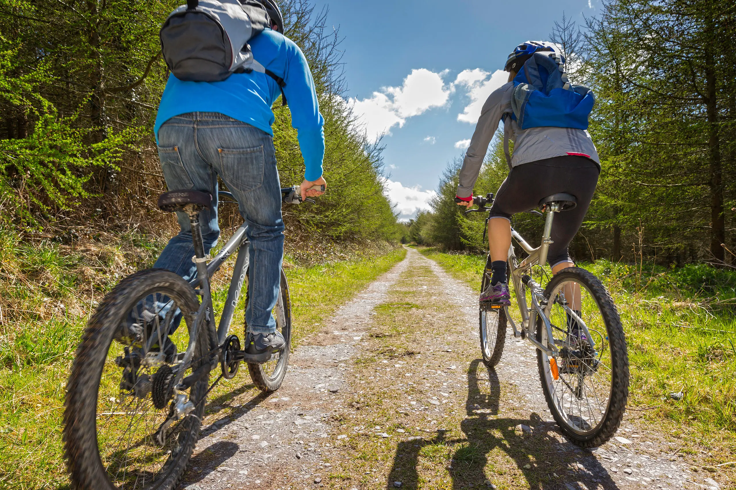 Two people cycling on a forest track with lovely clouds ahead