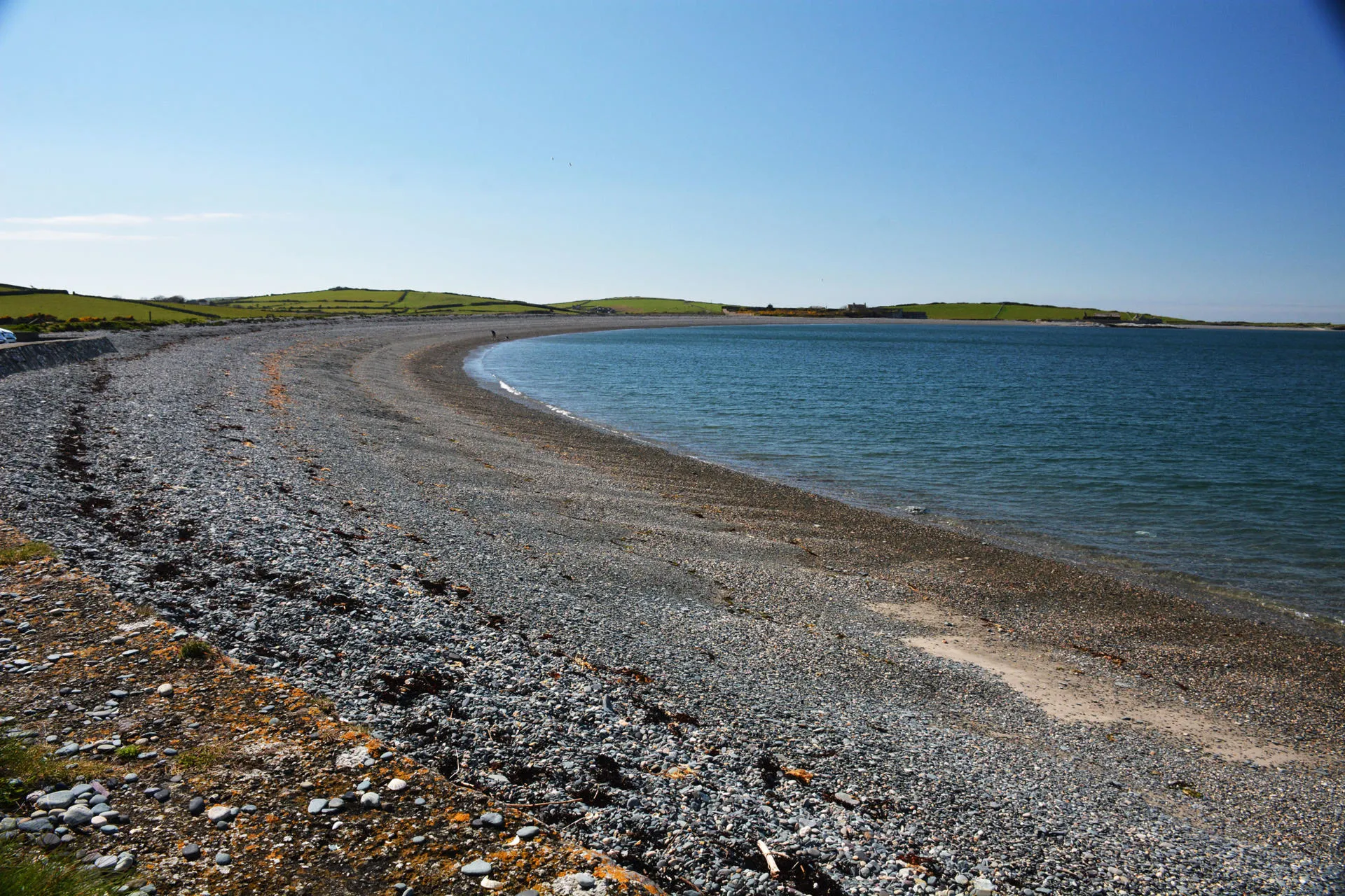Cemlyn beach with its shingle rock foreshore and blue lagoon to right.