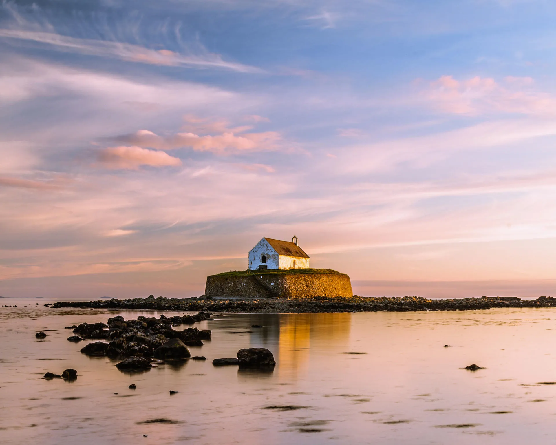A sunset scene of Llangwyfan church on a small island in a bay at low tide 