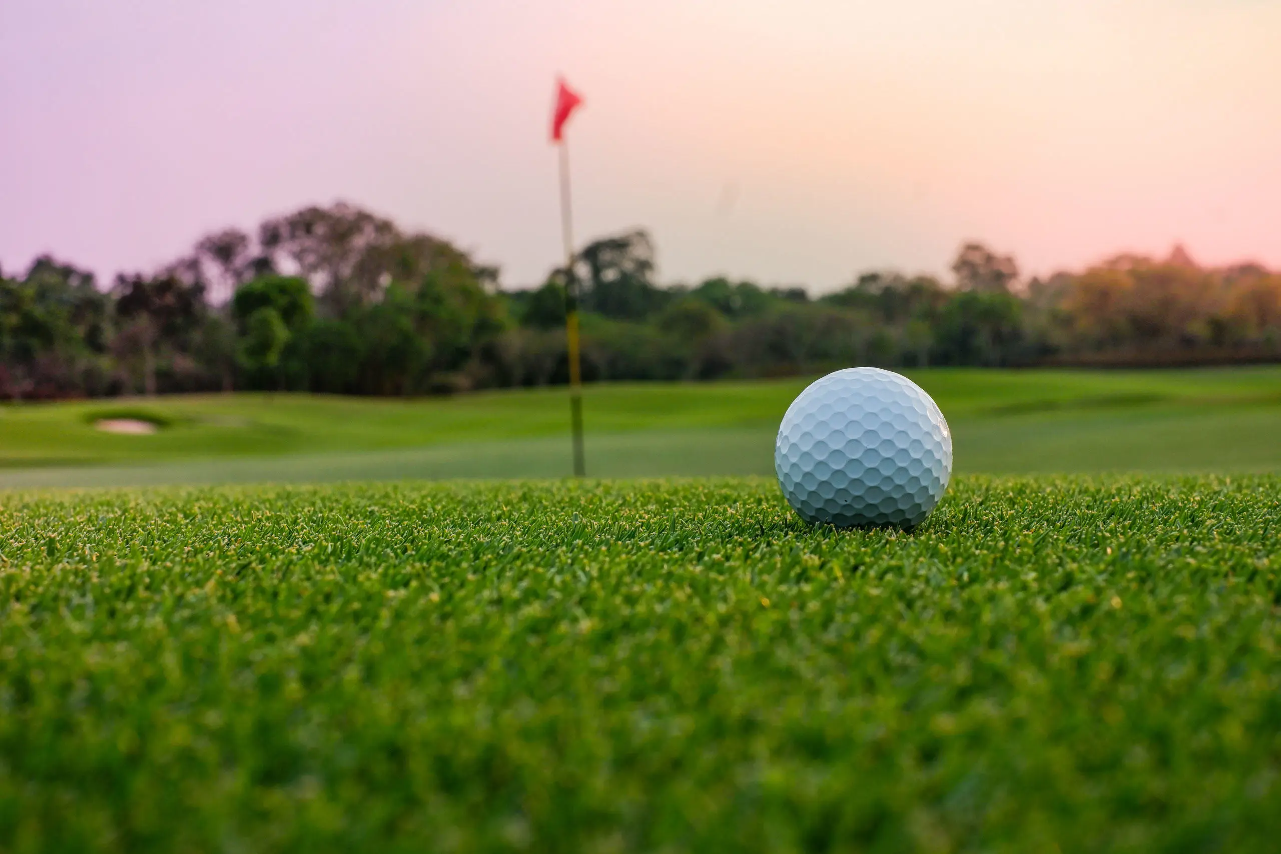 Early evening on the golf course. Ball on the green, red putting flag in the distance.