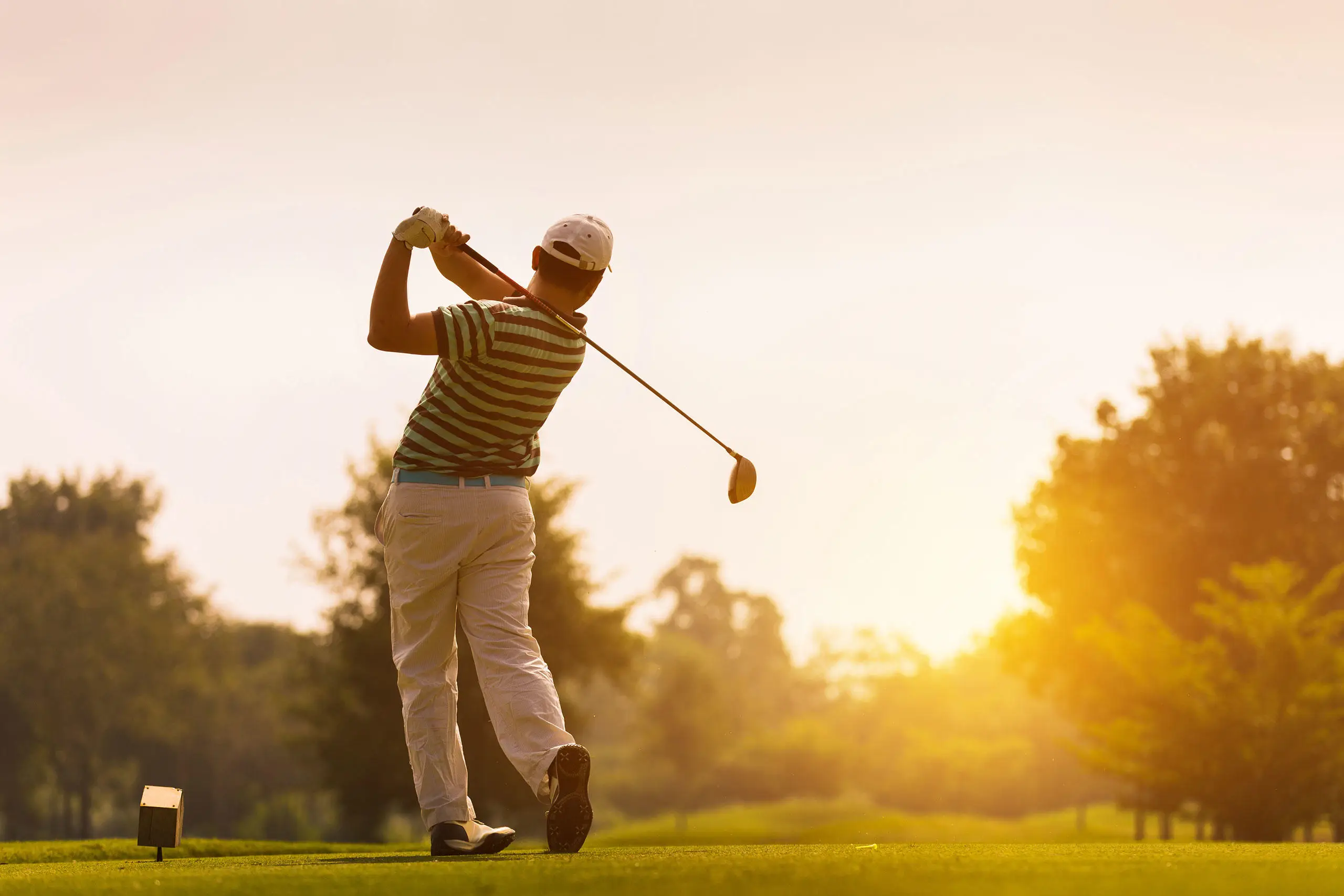 Person teeing off at sunset