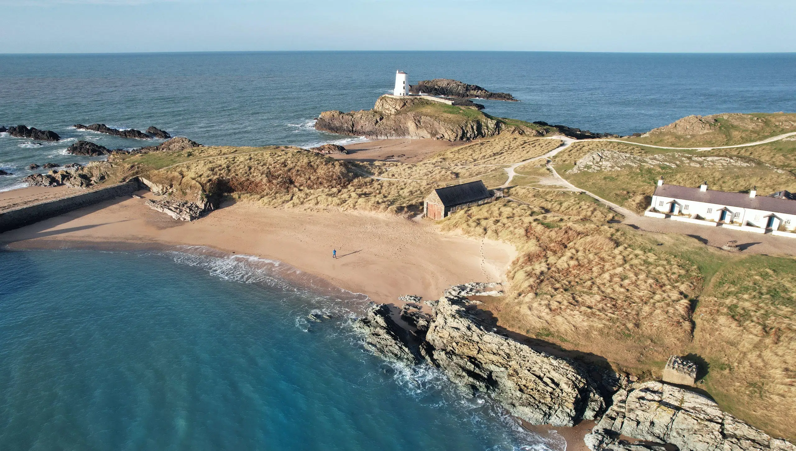 Ynys Llanddwyn i'w gweld o'r awyr gyda cherddwr unigol ar y traeth