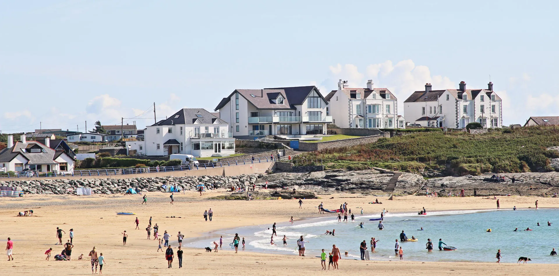 Houses in the background. A sunny day on the beach with lots of people on the sand and in the water